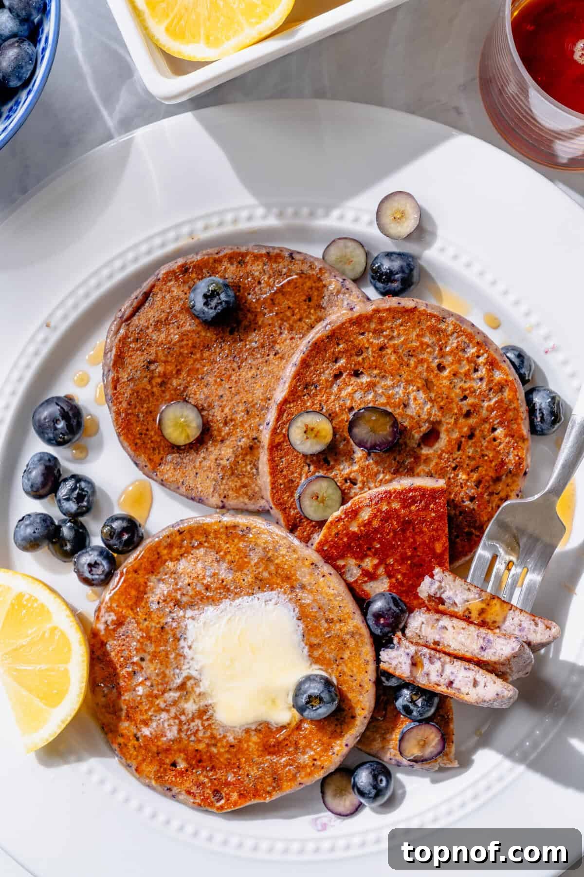 Zesty Lemon Blueberry Protein Pancakes 5 Stack of freshly cooked lemon blueberry cottage cheese pancakes on a white plate, garnished with fresh blueberries.