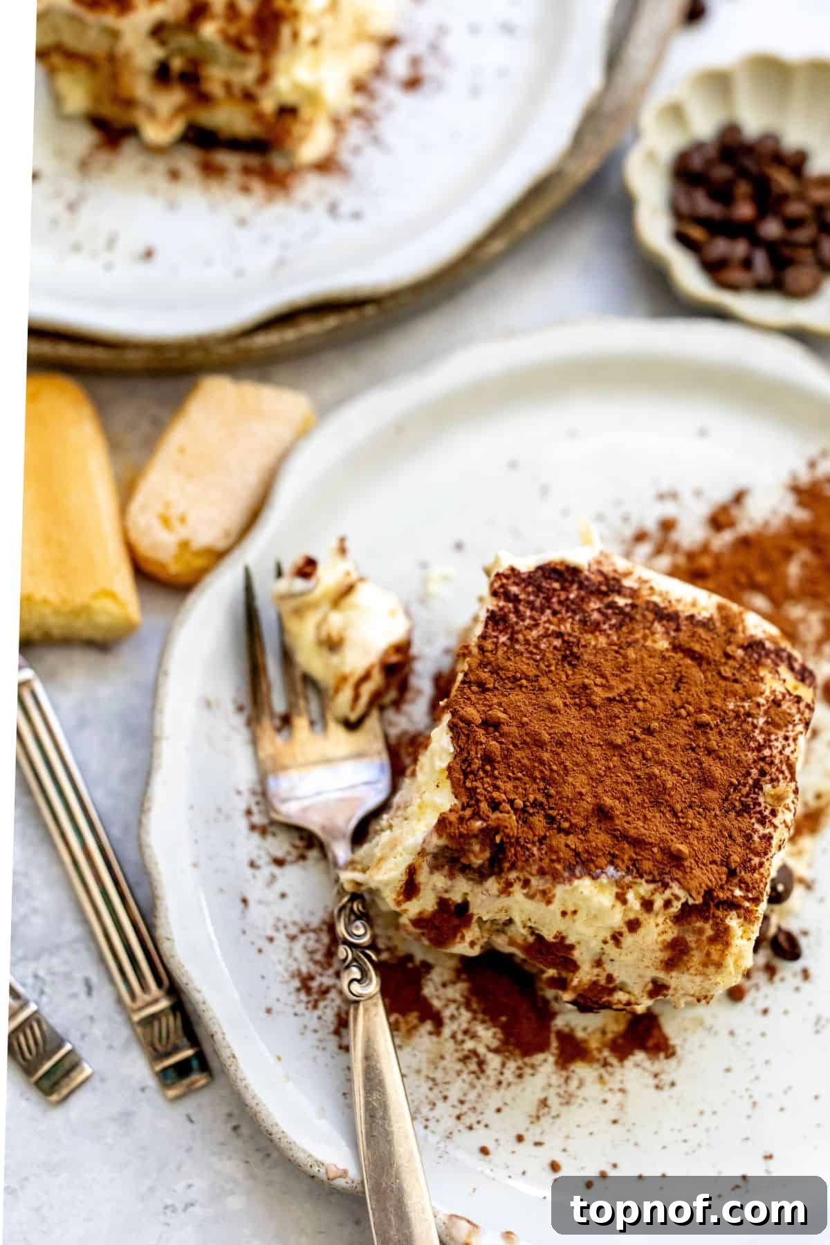 Decadent Protein Tiramisu 2 A perfectly portioned slice of tiramisu on a white plate, with a fork resting beside it, inviting a taste of its creamy layers and cocoa dusting.