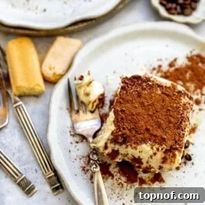 A close-up of a sliced tiramisu in a baking dish, showcasing its distinct layers of coffee-soaked ladyfingers and creamy filling, topped with a dusting of cocoa powder.
