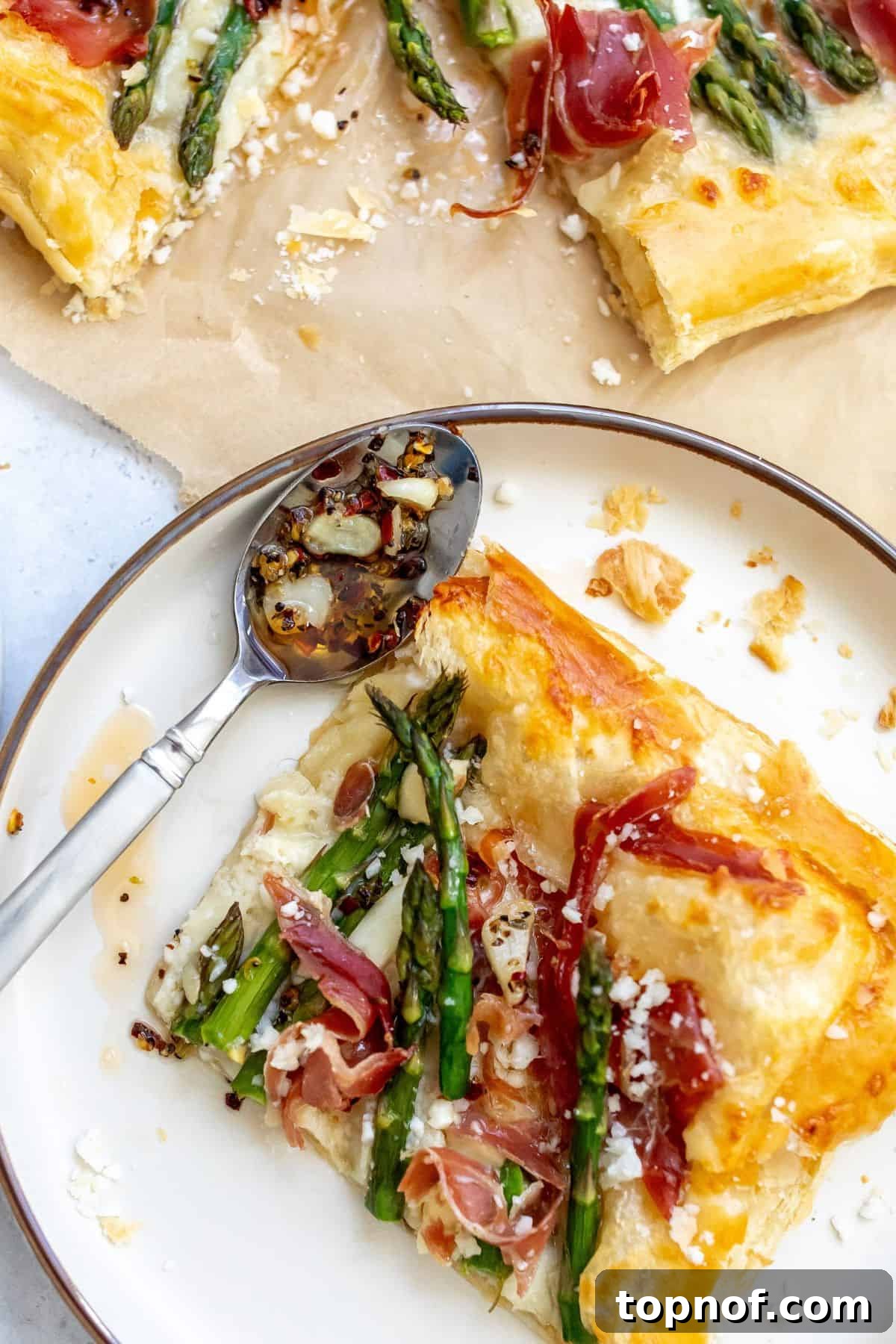 Golden Asparagus Bites 2 White plate with Asparagus puff pastry with prosciutto on it and a spoon to the side. A gourmet appetizer or easy meal.