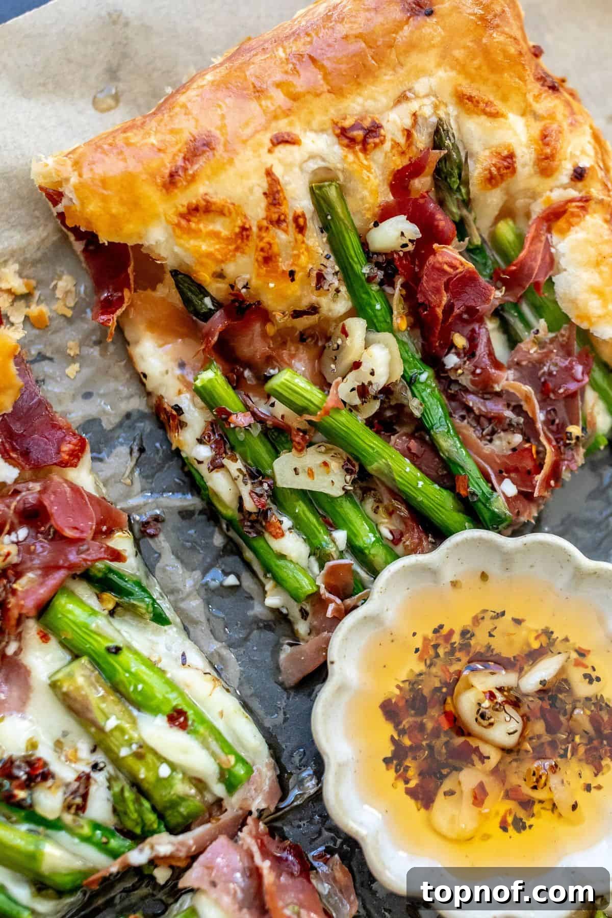 Golden Asparagus Bites 5 Asparagus puff pastry with prosciutto on it and a spoon to the side with oil and garlic, ready to be served.