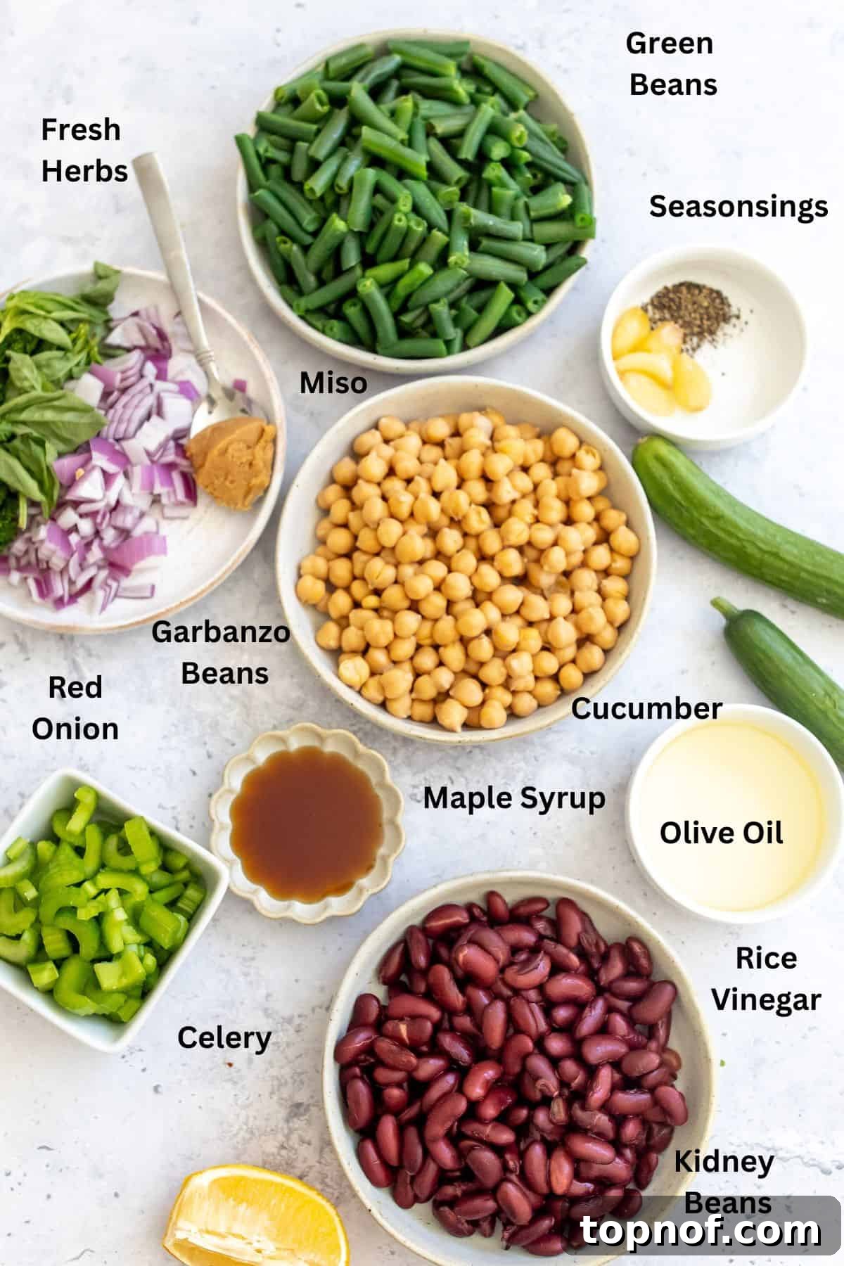Vibrant Miso Three Bean Salad 3 A collection of fresh ingredients for the three bean salad laid out on a kitchen counter in various bowls, including green beans, kidney beans, garbanzo beans, celery, cucumbers, red onions, and fresh herbs.