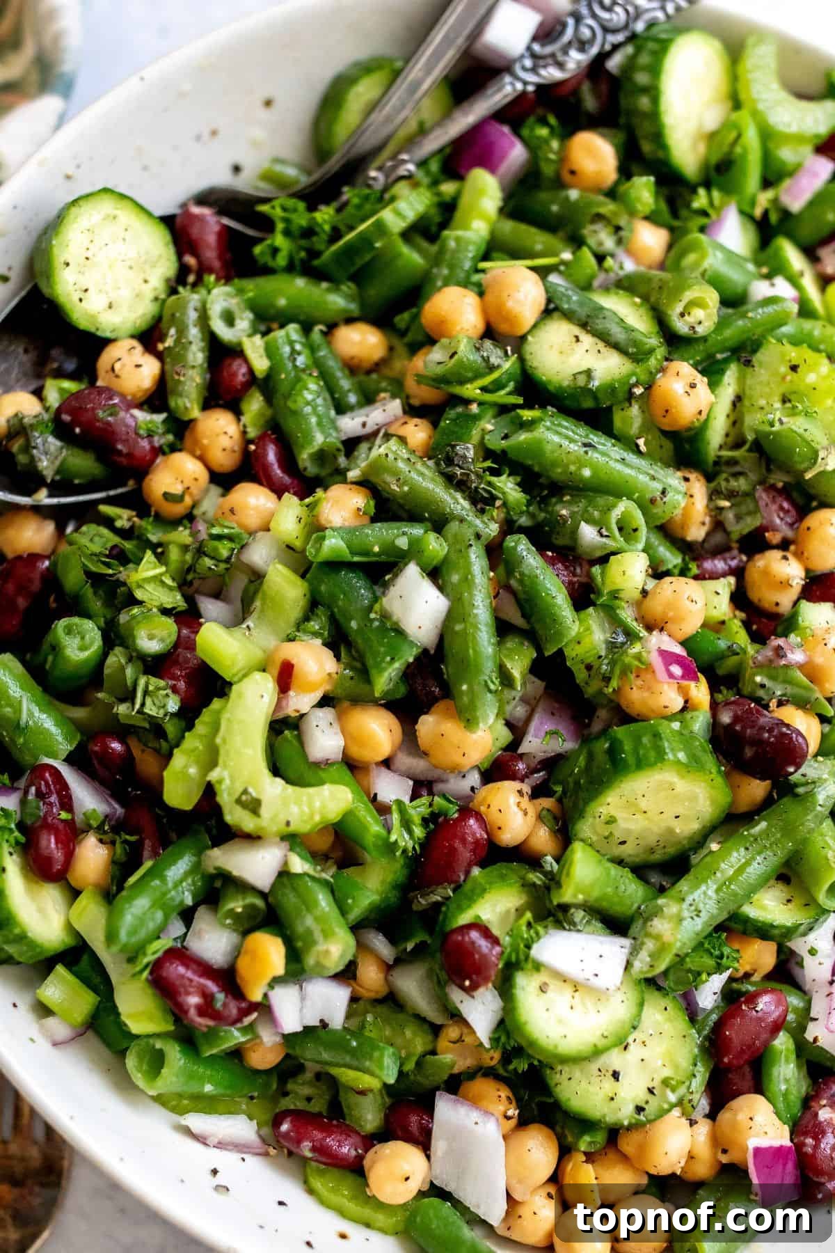 Vibrant Miso Three Bean Salad 5 A close-up view of the prepared three bean salad, generously sprinkled with cracked pepper and served with elegant silver serving spoons, highlighting its vibrant textures and inviting appeal.