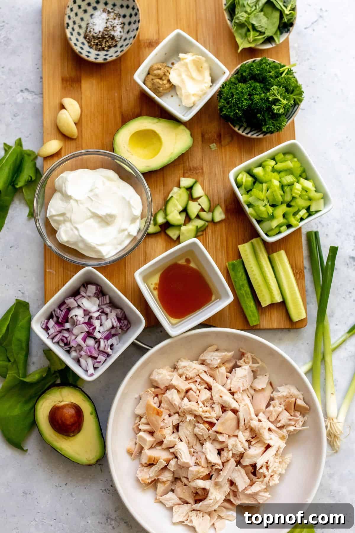 All the fresh ingredients required to make this Green Goddess Chicken Salad neatly arranged on a wooden cutting board in small bowls, ready for preparation.