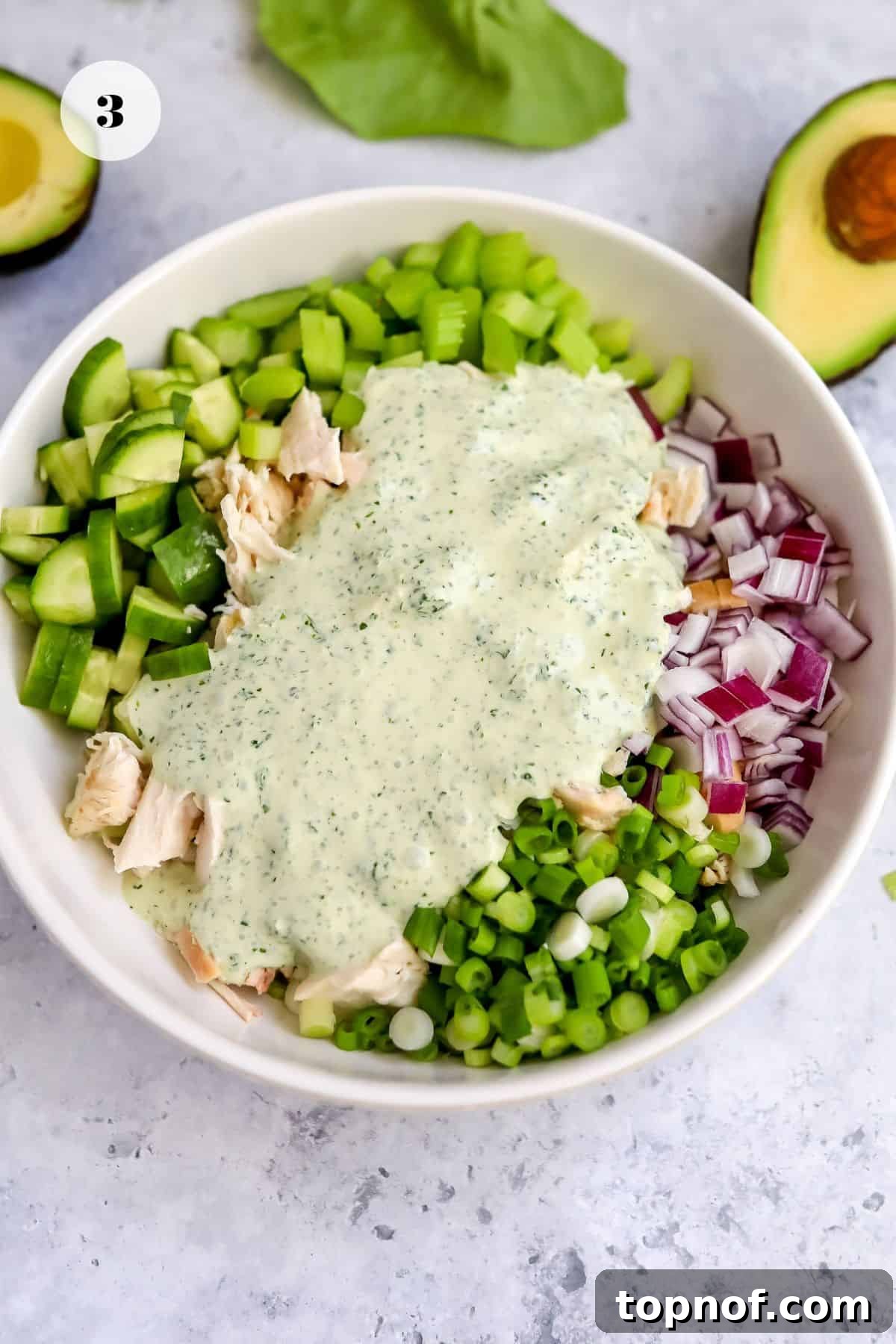 A large white bowl filled with the prepared chicken and chopped vegetables, awaiting the Green Goddess dressing.