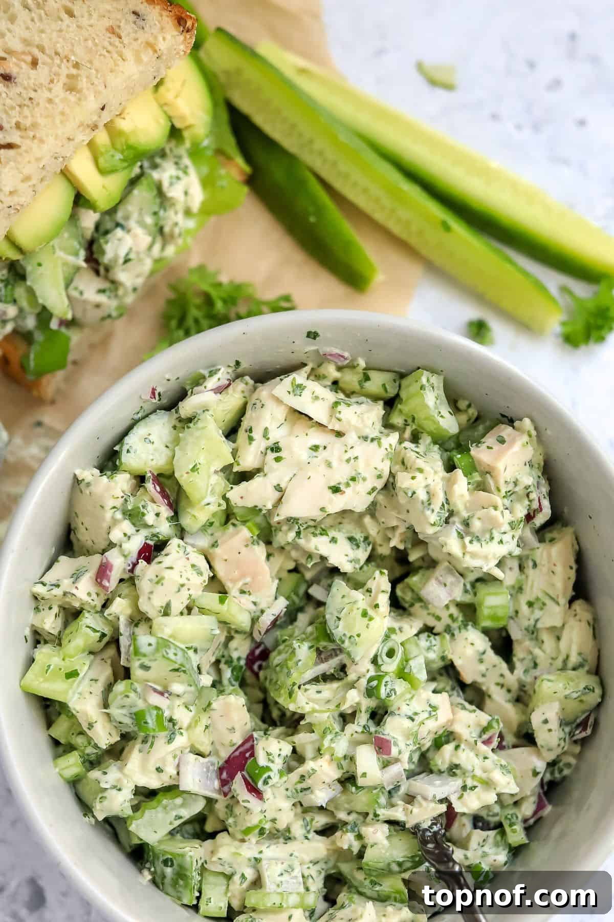 A serving of Green Goddess Chicken Salad in a white bowl, with a prepared sandwich featuring the salad on the side, ready to be eaten.