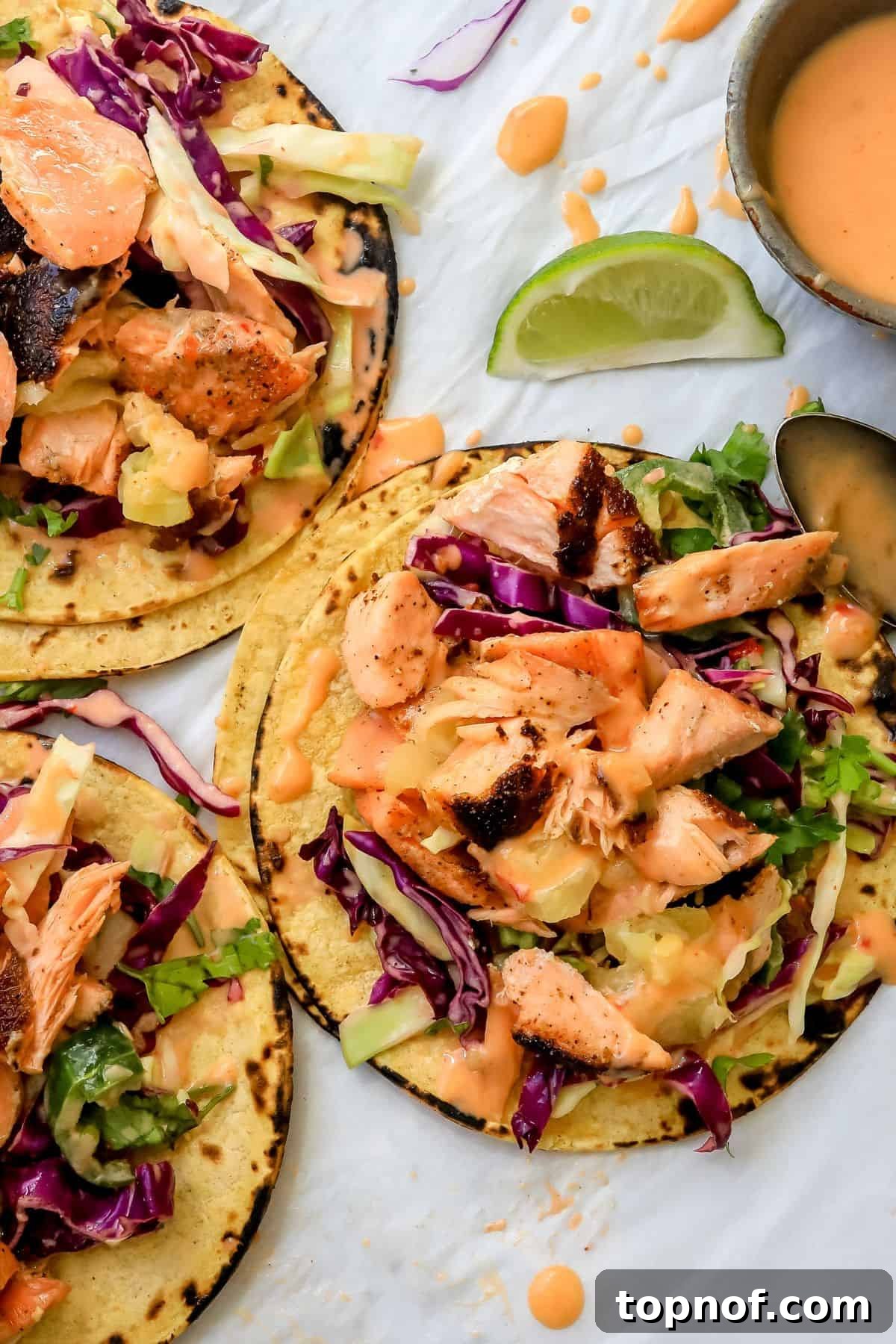 Firecracker Salmon Tacos 2 Bang Bang Salmon Tacos on parchment paper with sauce and limes on the side, highlighting their vibrant appearance.