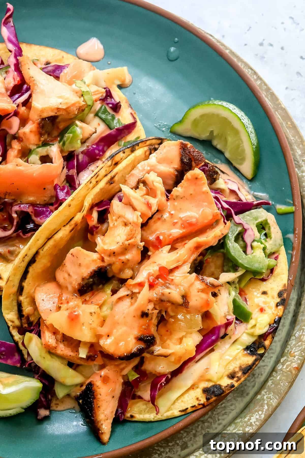 Firecracker Salmon Tacos 5 Bang Bang Salmon Tacos presented on a vibrant green plate, with extra sauce and a squeezed lime for garnish.