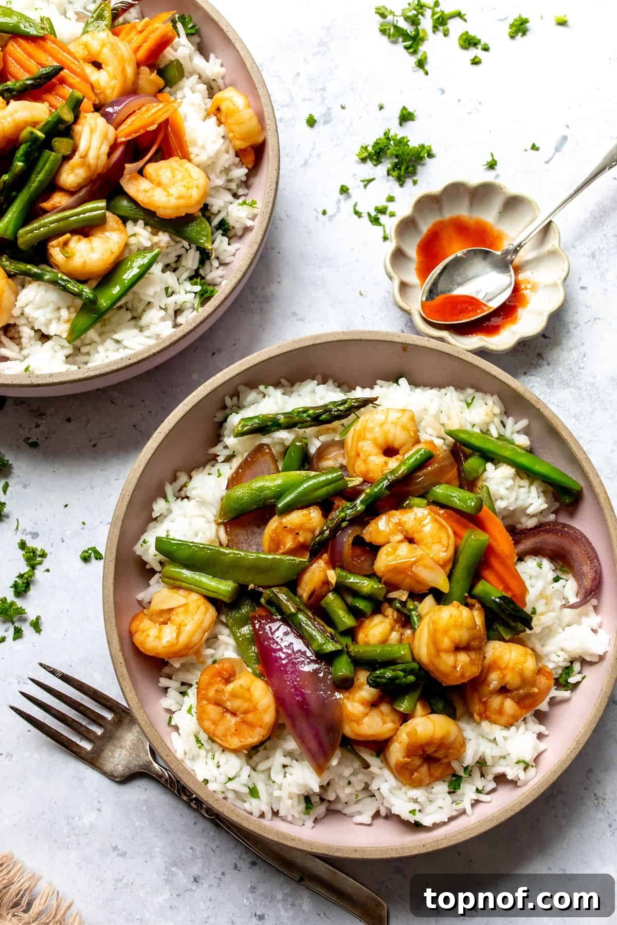 Garlic shrimp stir fry served over white rice in pink bowls with forks to the side. A vibrant, healthy, and delicious family meal.