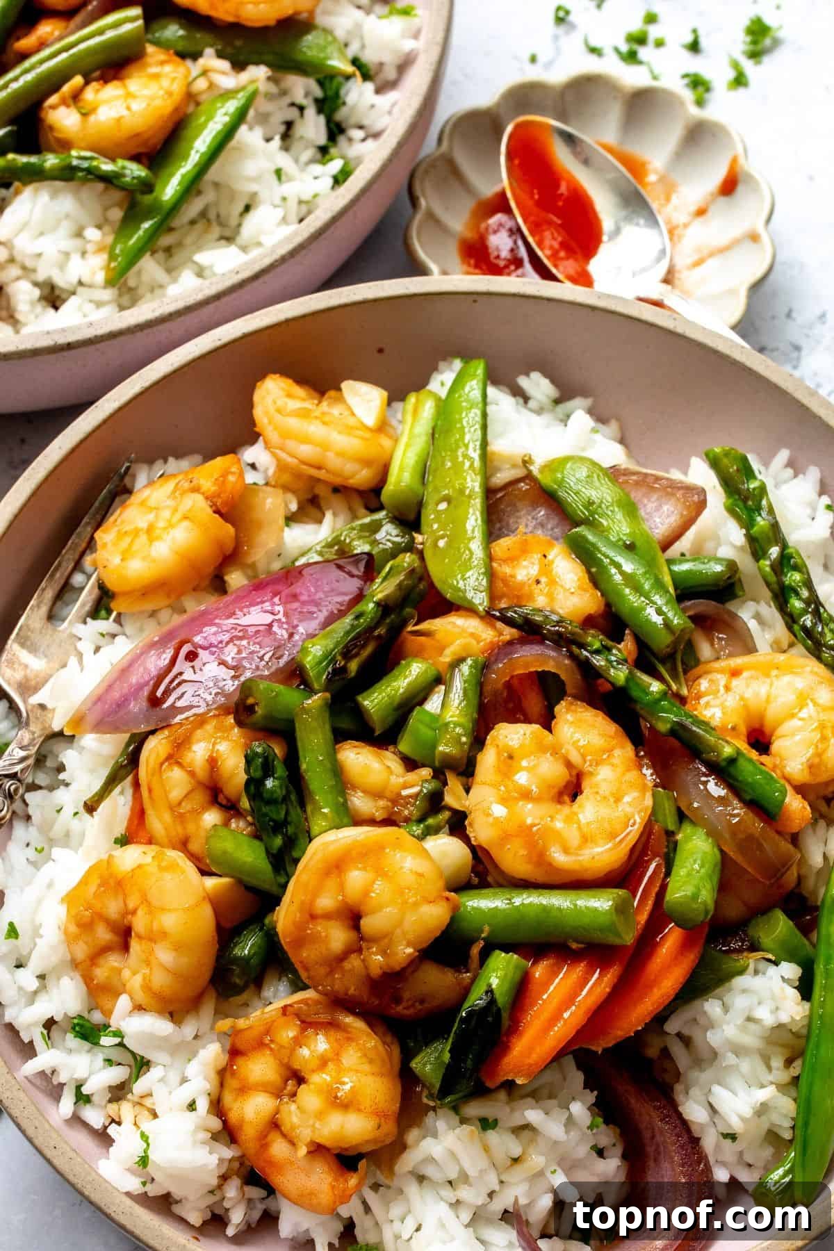 Close-up of a pink bowl filled with garlic shrimp stir fry and white rice, with a fork resting beside it, highlighting the vibrant colors and appealing texture of the meal.