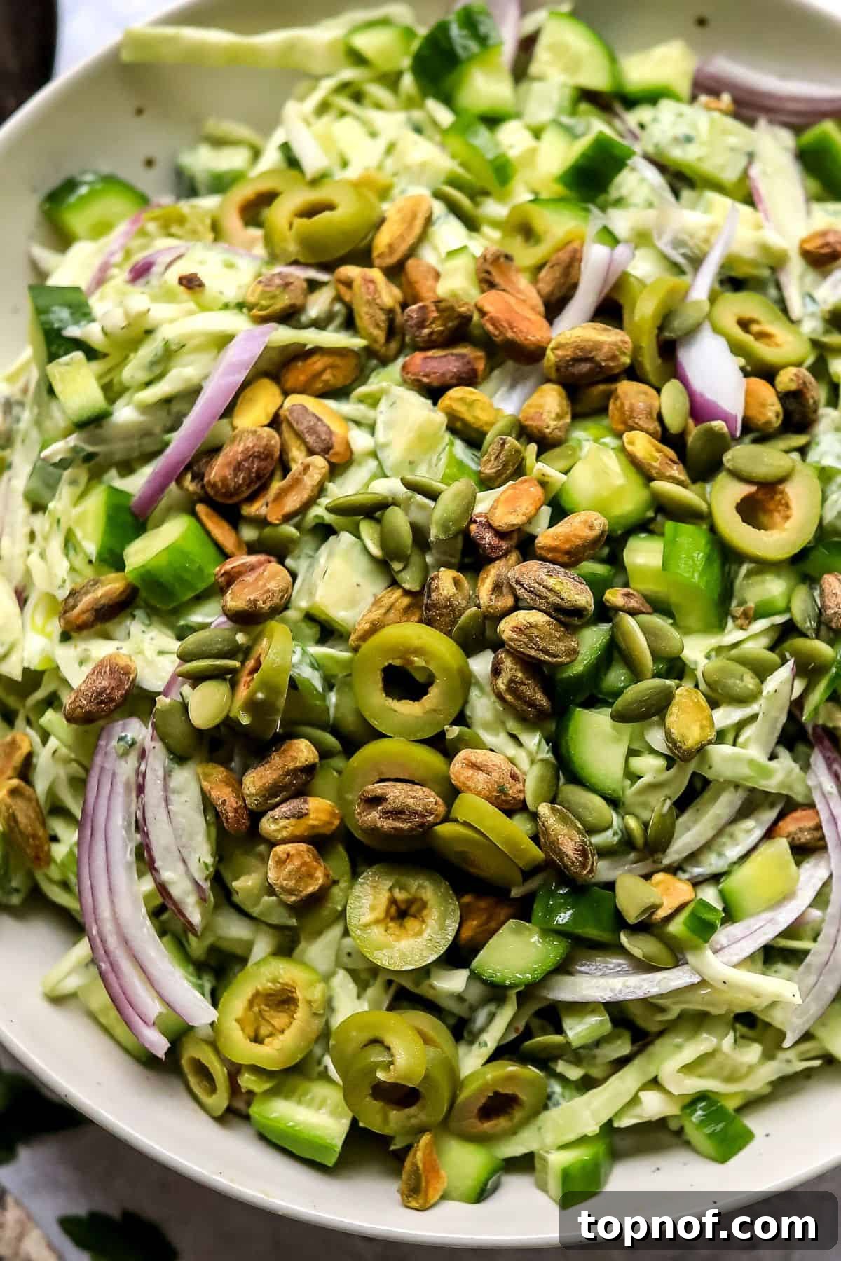 Emerald Goddess Salad 4 A small blender containing the creamy green goddess dressing, with chunks of avocado visible, indicating the blending process. A portion of the finished salad is blurred in the background, ready for dressing.