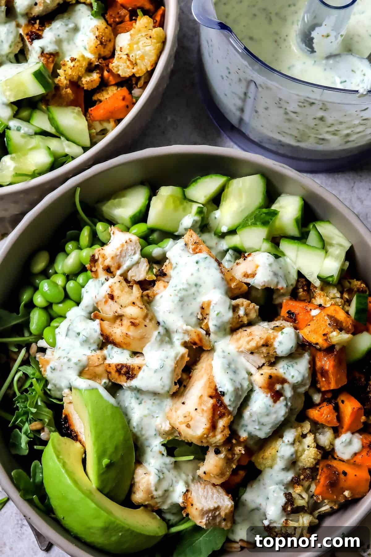 Lemon Garlic Chicken Grain Bowls with Roasted Veggies 5 Grey bowls with chicken power bowls in them and dressed with sauce up close.