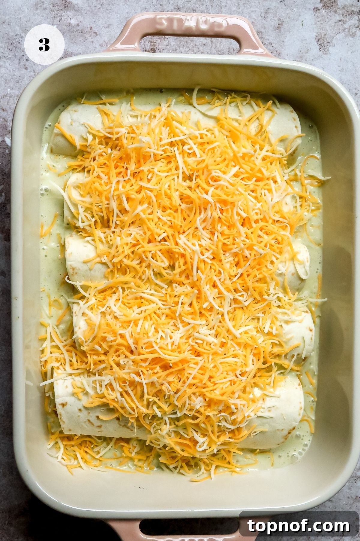Poblano Chicken Enchiladas Recipe with Creamy Cheese Sauce 5 Enchiladas in a pink baking dish with lots of shredded cheeses on top before going into the oven.