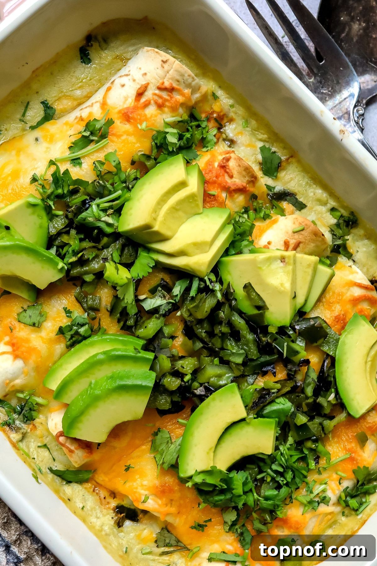 Poblano Chicken Enchiladas Recipe with Creamy Cheese Sauce 6 Poblano Chicken Enchiladas in a baking dish with avocados and peppers on top.