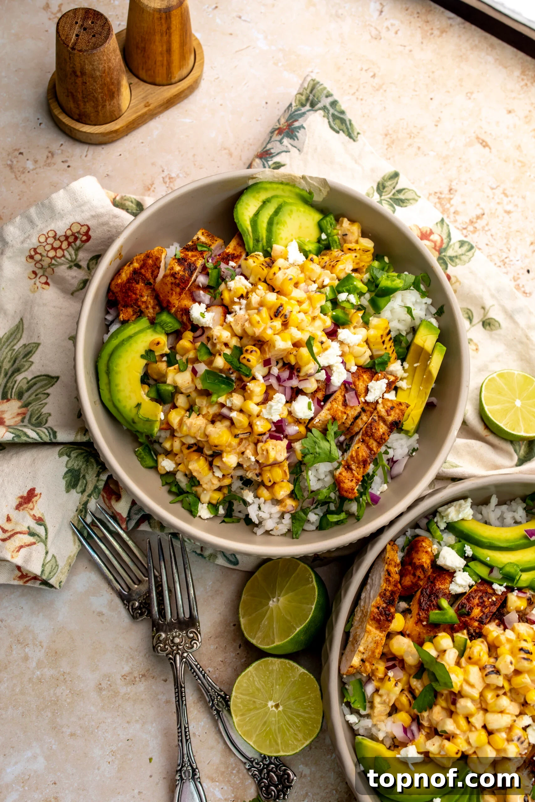Street Corn Chicken Rice Bowls with Lime Crema 2 Street Corn Chicken Rice Bowls in a grey textured bowl. Limes on the side with forks.