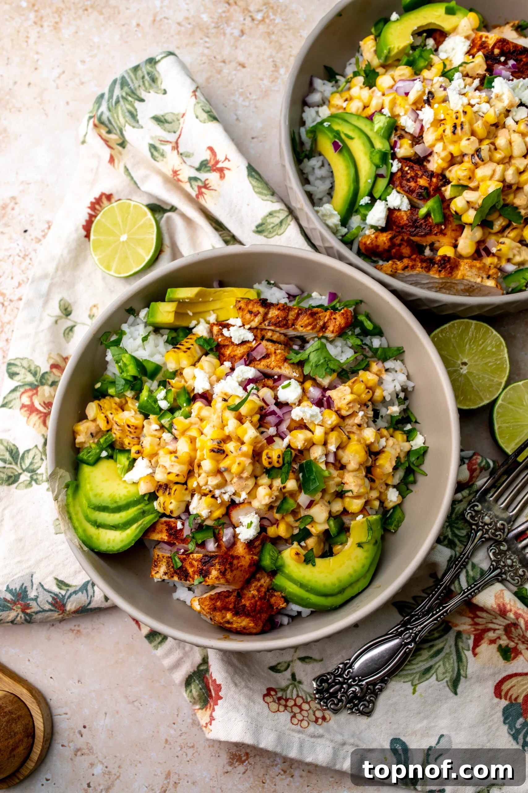 Street Corn Chicken Rice Bowls with Lime Crema 6 Two Chicken Street Corn Rice Bowls on a counter with a floral napkin underneath and silver forks to the side.