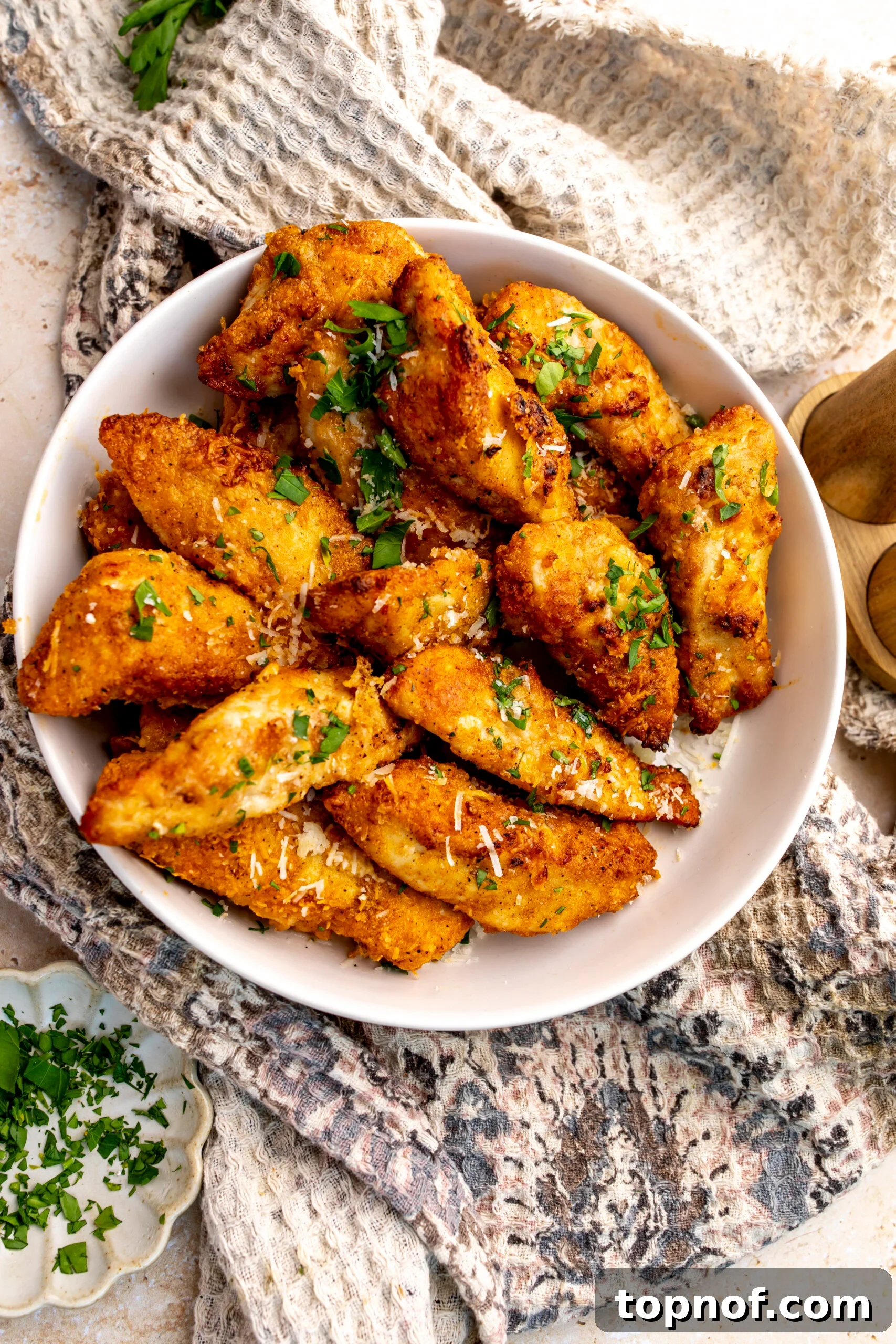 Crispy Garlic Parmesan Chicken Tenders Recipe 2 Golden Garlic Parmesan Chicken Strips in a white bowl topped with parsley.