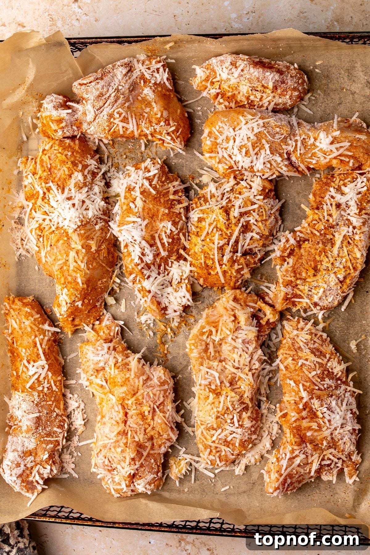 Crispy Garlic Parmesan Chicken Tenders Recipe 4 Chicken strips with coating and Parmesan cheese on top on parchment paper.