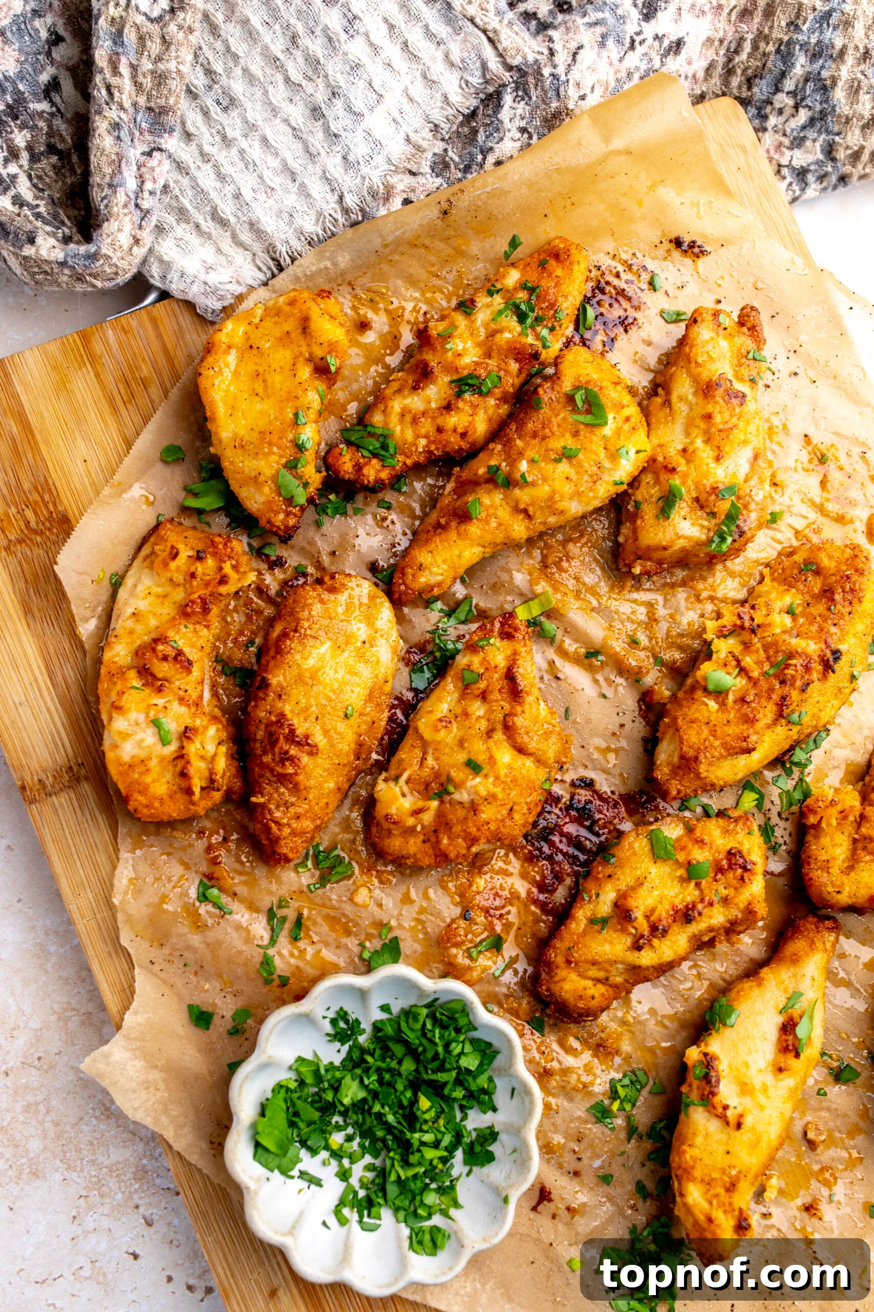 Crispy Garlic Parmesan Chicken Tenders Recipe 5 Golden Garlic Parmesan Chicken Strips on brown parchment paper with parsley on top.