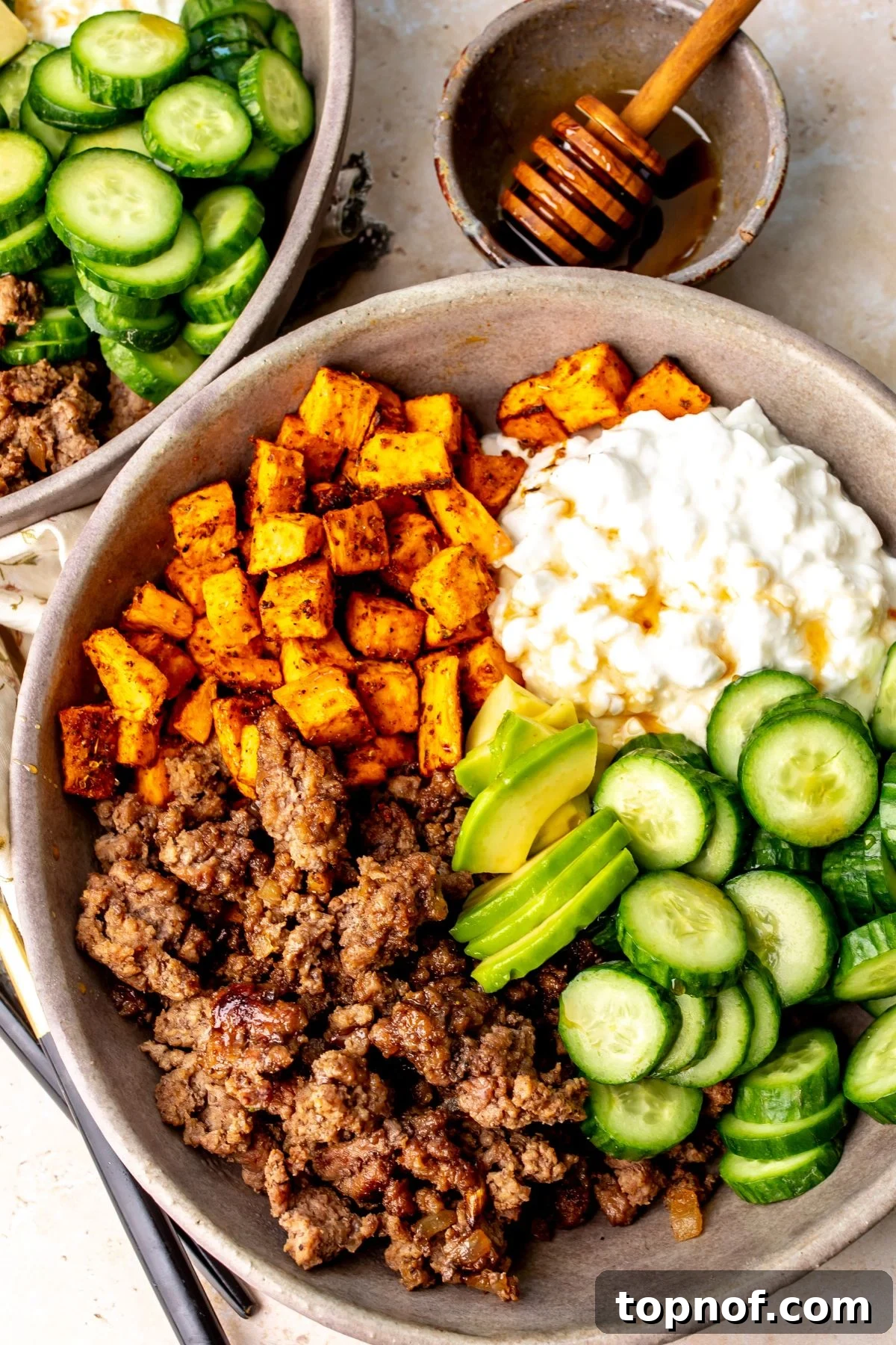 Spicy Honey Glazed Ground Beef Bowls 4 Hot honey ground beef bowls with sweet potatoes, avocado, cucumbers, and cottage cheese in a bowl on a countertop.