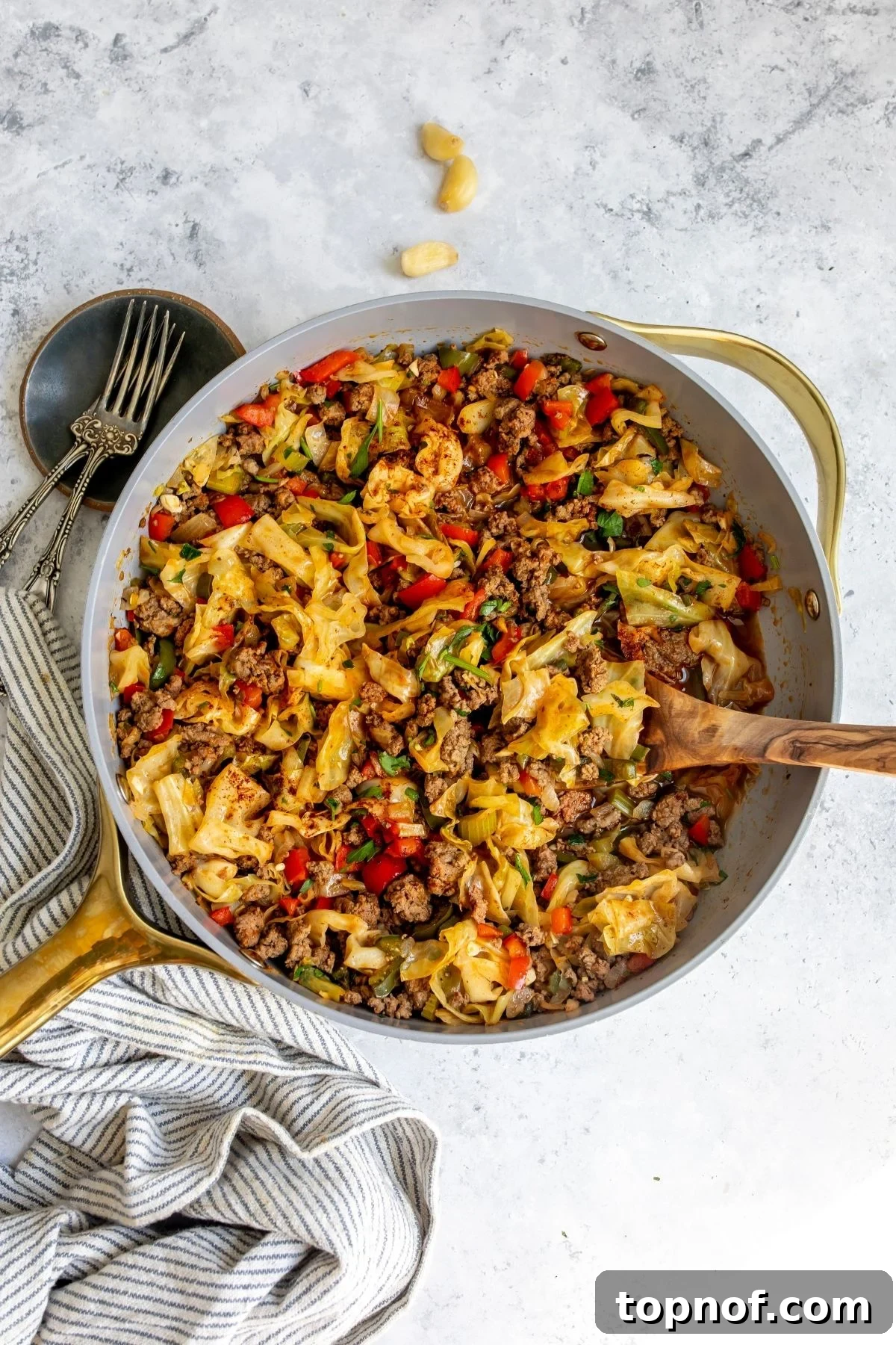Dirty Cabbage: Spicy Skillet Cabbage with Bacon 2 Dirty cabbage in a grey pan with a wooden spoon and a towel to the side.