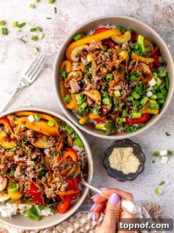 Two white bowls with ground beef stir fry in it and sauce to the side.