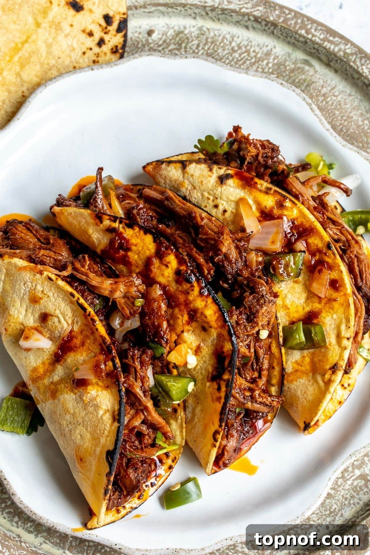 Slow Cooker Beef Birria Tacos with Dipping Consomme 9 Three birria tacos on a white plate for serving.