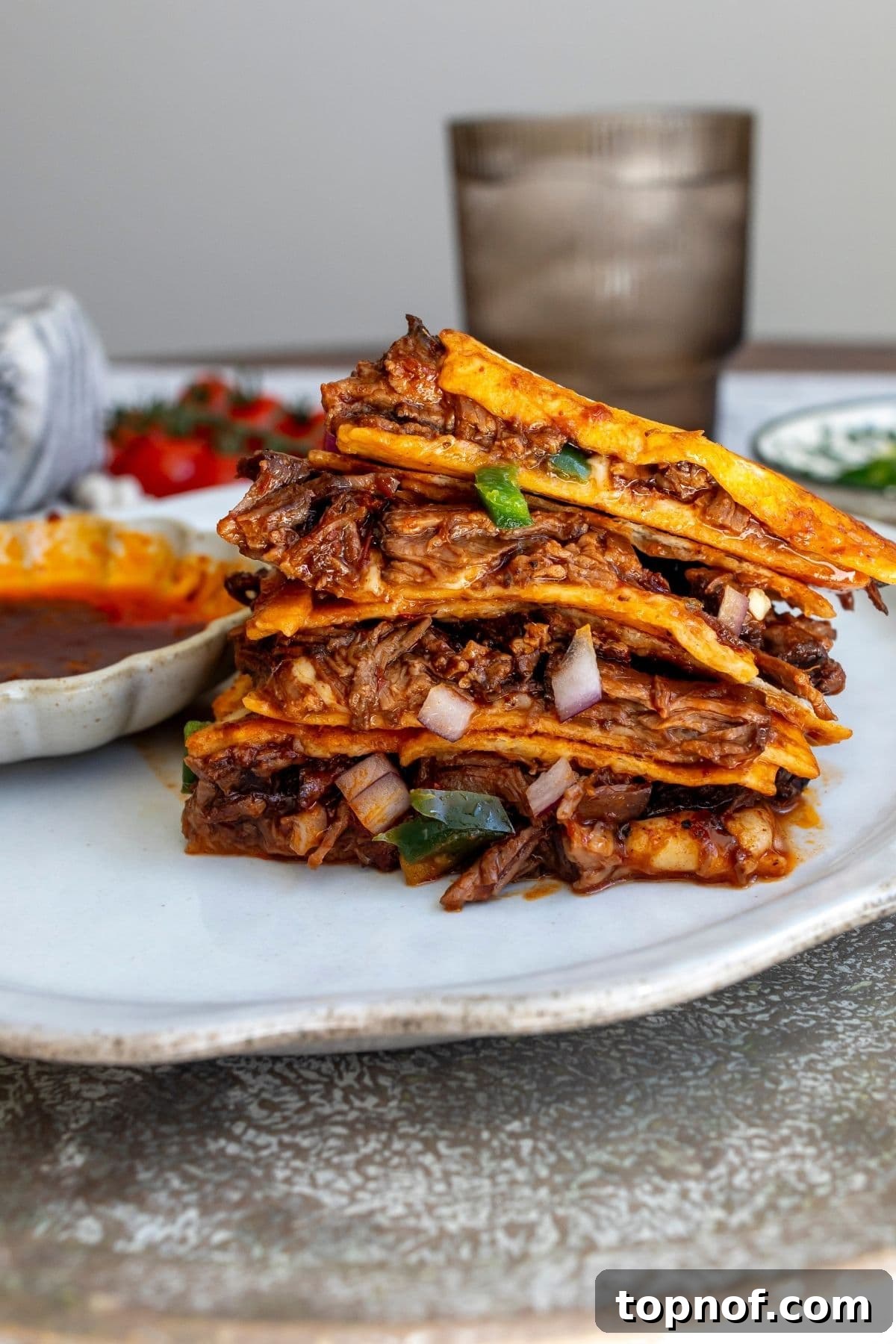 Birria Quesadillas with Dipping Consomme 5 Birria quesadilla sliced into four large pieces and stacked on a plate with a bowl of the extra comsomme to the side.