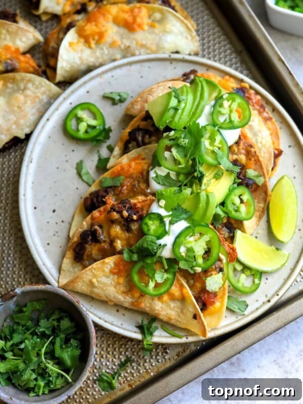 Crispy Black Bean Tacos on a white plate with limes and cilantro, sour cream and jalapeño.